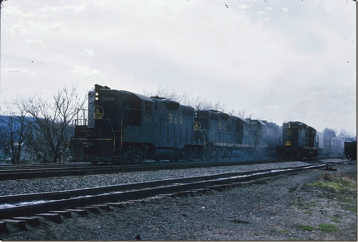 B&O 5966-6433-4810-5963-5957 accelerate out of town with an e/b “QD” (as B&Oers call a freight train). GP9 6488 waits on the right. Clarksburg.