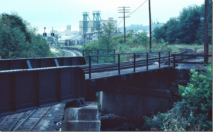 The eastern-most bridge passes over the Parkersburg SD. The track leading off the MR to the left joins the WV&P SD and goes to the depot. J Tower was just beyond the bridge on the right of the main line. You can see under the bridge that double track is reducing to single going west. B&O Clarksburg.