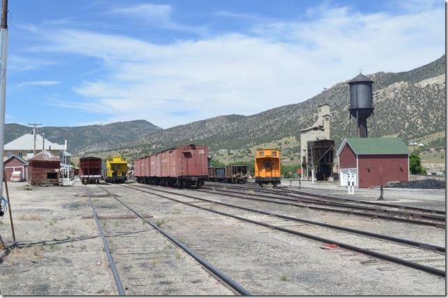 Nevada Northern’s East Ely Yard looking west. Left to right are the depot, team track, main line with yellow caboose, vintage boxcars, Kennecott Copper orange caboose, coal dock, and water tower. The nearest building to the depot housed the dispatcher.