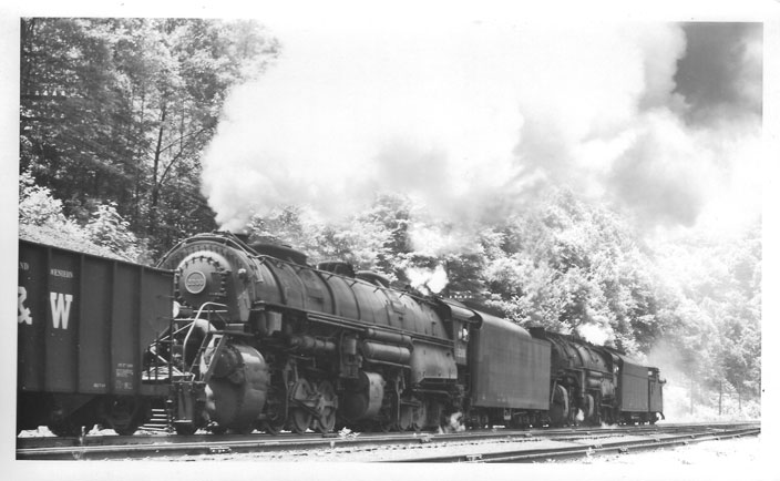 Mallets 2200-2147 move down the main line of the Buchanan Branch to serve as pushers for the coal train on the left. The bunk house is in the background. The symmetry of the hoppers and the coal would make this a company photographer's dream!
