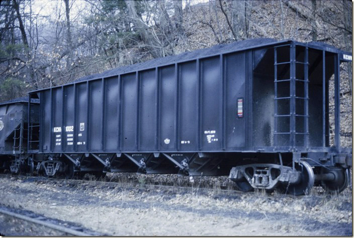 KC&NW 1002 was owned by Valley Camp Coal. Although equipped with an ACI (Automatic Car Identification) plaque, it is doubtful the car ever left home rails. It was confined to shuttle service between the mine and the barge terminal on the Kanawha River. Being in captive service probably explains the plain bearing trucks. The railroad is gone now. 1972.
