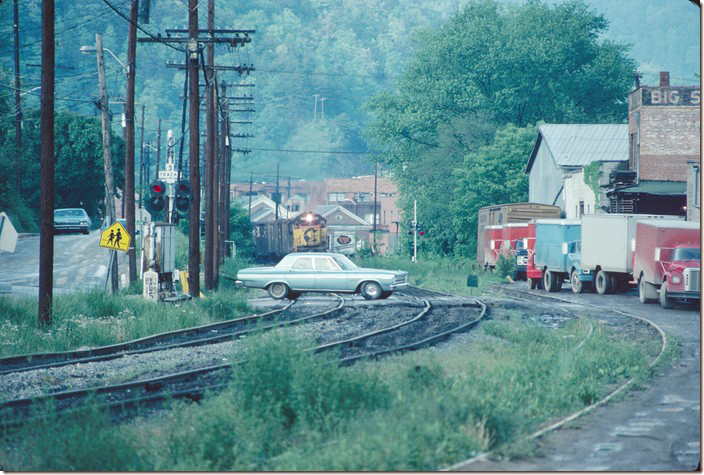 Eastbound C&O manifest freight No. 192 comes slowly through town as a car crosses the Elm Street crossing beside Big Sandy Wholesale. 05-10-1978. Pikeville KY.