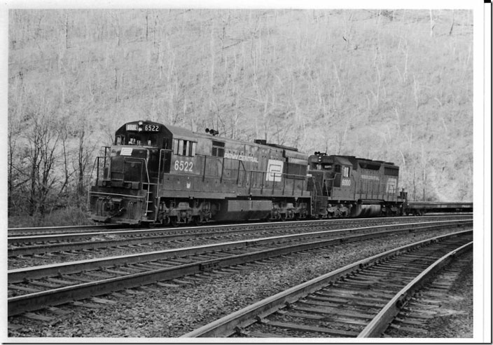 Lowell Suttman and I were able to beat the slow moving freight to “The Curve”, run up the steps and get PC U-28C 6522 and “class” SD35 6000 growling past on track 4 (westbound freight track). The U28Cs were part of PRR’s 1966 engine order that included the 2800 HP U28C, the 3000 HP ALCo C-630 and the 3600 HP EMD SD45. The last few GEs on the order were delivered as 3000 HP U30Cs. The SD35s were part of the 1965 order and numbered 40 units. Horseshoe Curve.